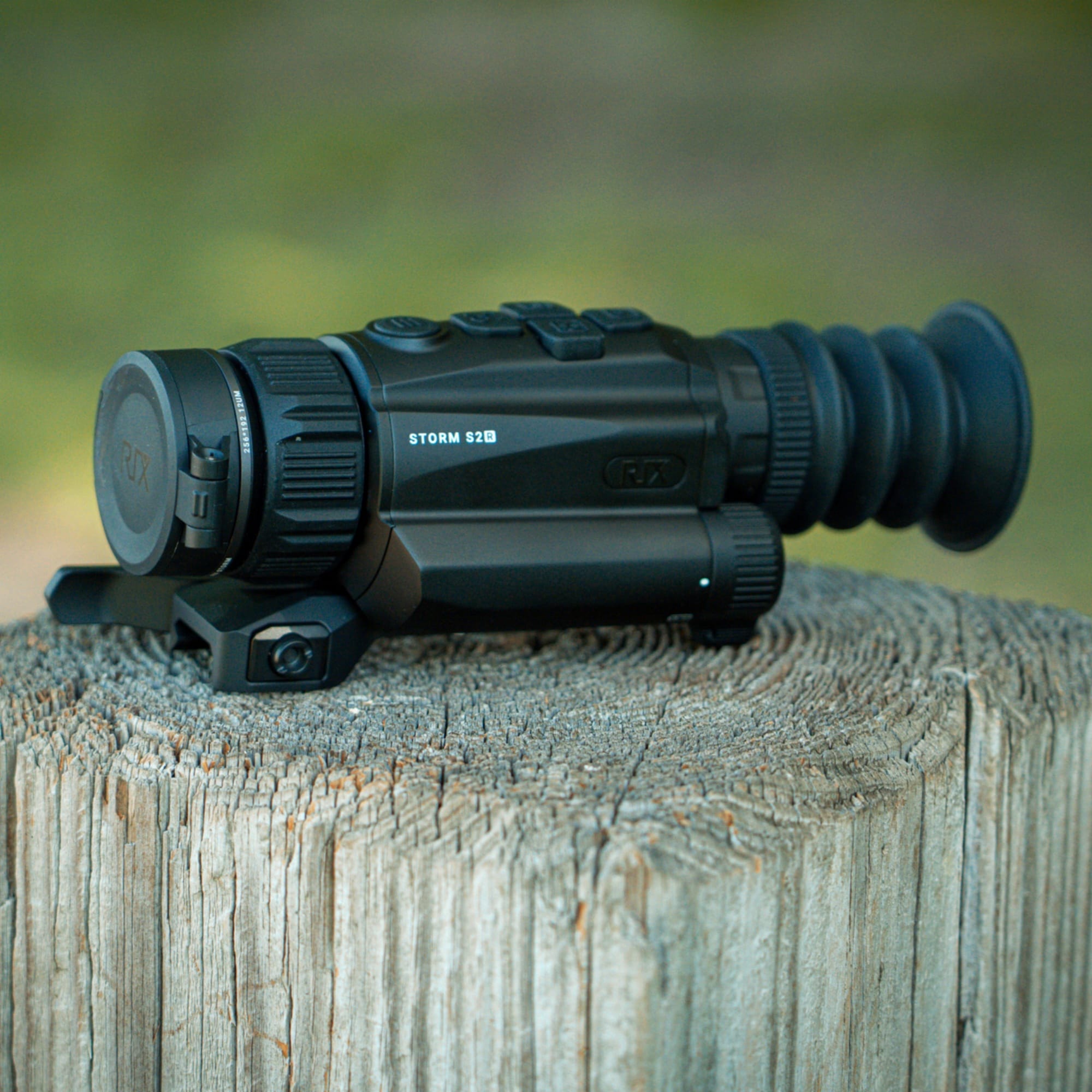 A rifle scope resting on a weathered wooden surface outdoors, close up of the eyepiece and adjustment knobs.
